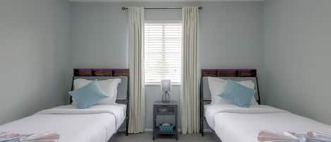 Habitación doble con dos camas, una mesita de noche, una ventana con cortinas y vistas al exterior.