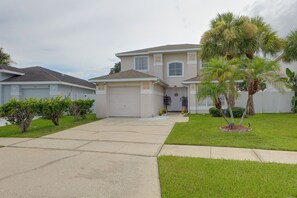 A two-story house with a garage, a front lawn, and a palm tree. - Kissimmee Family Fun w/ Private Pool & Pond Views! (Kissimmee)