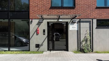 Entrada de un edificio con puerta de vidrio, detector de incendios y cartel con la dirección.