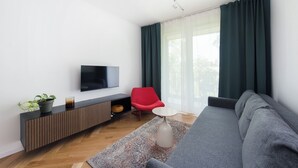 Una sala de estar moderna con un televisor de pantalla plana, una silla roja, un sofá gris y un ventanal con cortinas.