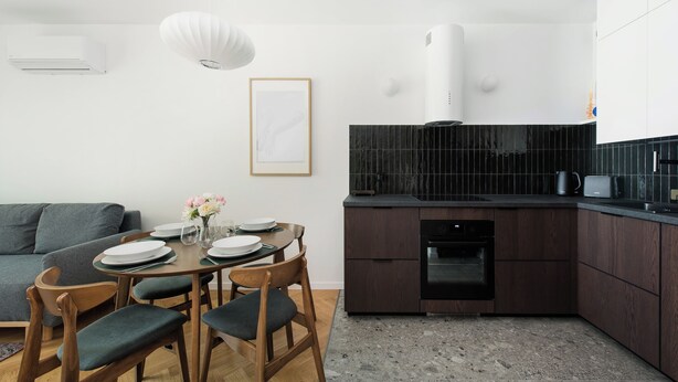 Una cocina moderna con armarios de madera oscura, encimera negra y horno integrado.