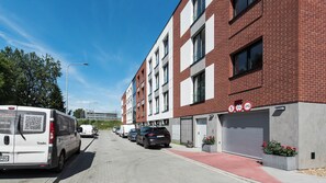 A street view with a multi-story building, parked cars, and a QR code on a white van. - Apartamenty Sun & Snow Old Podgórze (Kraków)