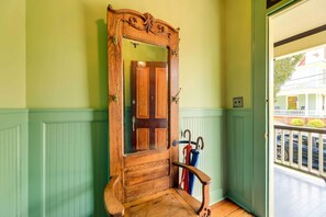 A wooden door with a mirror, a wooden bench, and a coat rack with umbrellas. - Twin Victorian Apts in Downtown New Bern (New Bern)