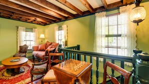 A room with a wooden table set for a game, a sofa, and chairs, with a view of the outdoors through large windows. - Twin Victorian Apts in Downtown New Bern (New Bern)