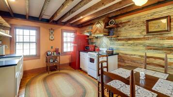 Una cocina con vigas de madera, un refrigerador rojo, una estufa y una mesa de comedor con sillas.
