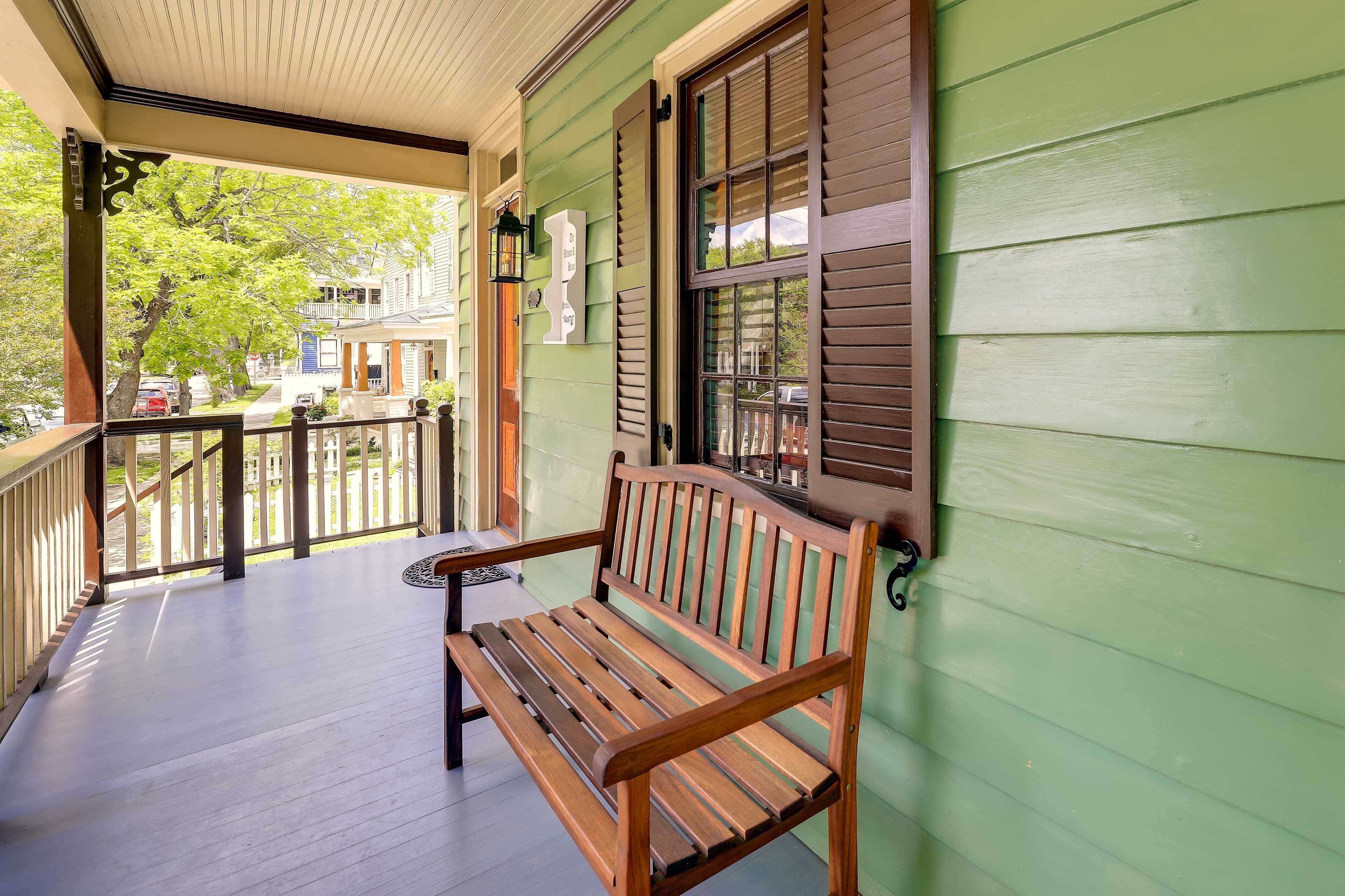 A wooden bench on a porch with a green wall and a window with shutters.