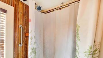 Ein Duschbereich mit Holzwand, einem weißen Duschvorhang mit Pflanzenmotiven und einem Metallgriff.
