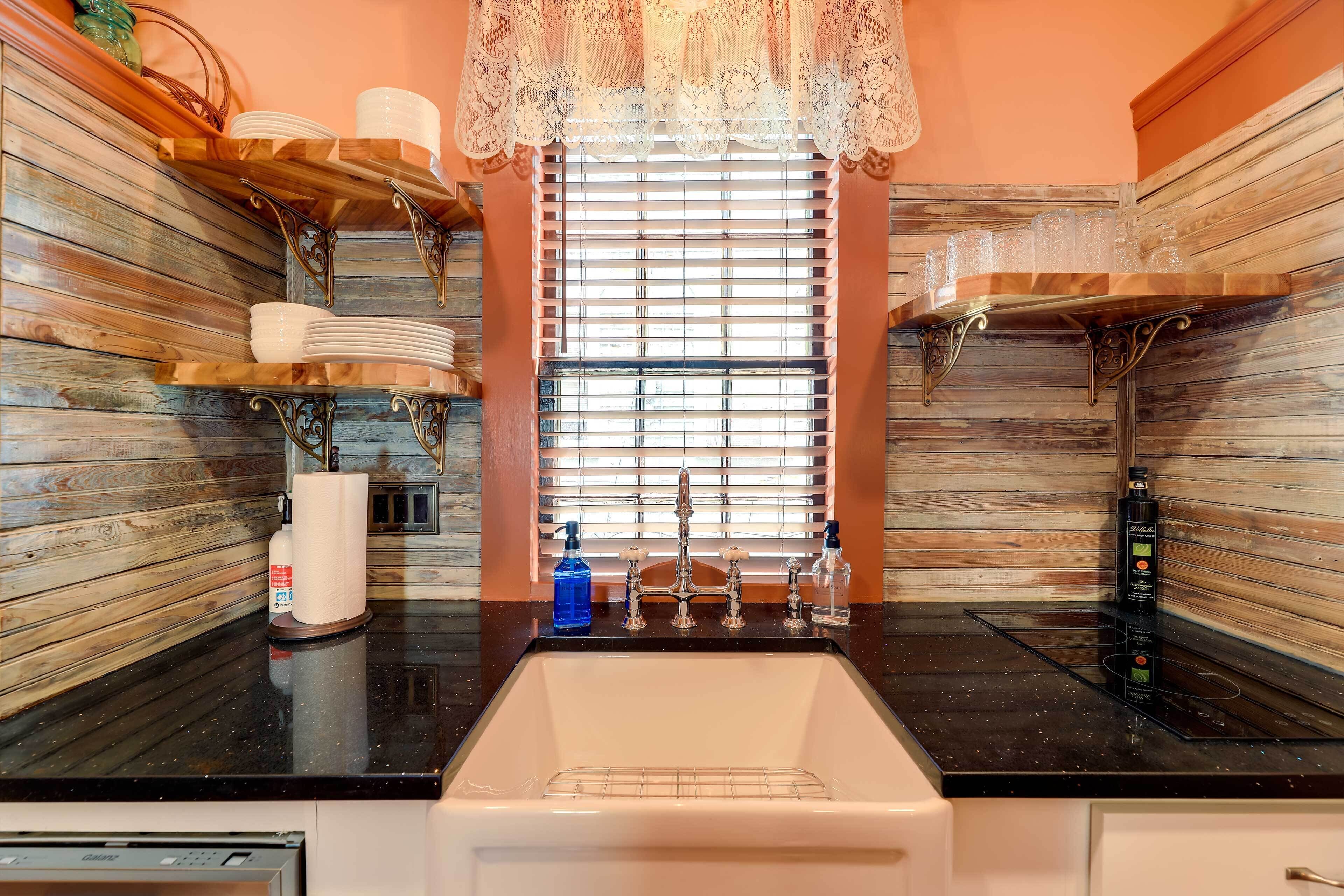 A kitchen with a black countertop, a white sink, and a window with blinds.