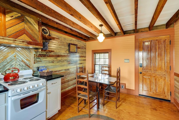Una cocina con vigas de madera, estufa y una mesa de comedor con sillas.