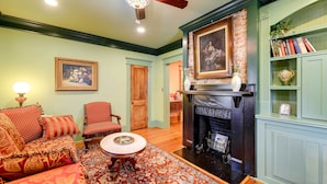 A cozy living room with a fireplace, a sofa, a chair, and a bookshelf. - Twin Victorian Apts in Downtown New Bern (New Bern)