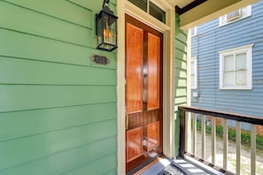 Una casa verde con una puerta doble de madera y un farol negro en la pared.