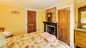 A bedroom with a bed, a fireplace, wooden doors, and a dresser. - Twin Victorian Apts in Downtown New Bern (New Bern)