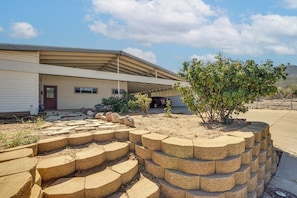 Una casa de dos pisos con un porche cubierto, un automóvil estacionado en la entrada y un jardín con un árbol y escalones de piedra.
