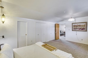 A bedroom with a bed, a wooden tray, a white wall, a painting, and a hallway leading to another room. - Walkable Home in Cedar City With Ample Parking (Cedar City)