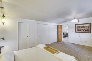Un dormitorio con una cama, una bandeja de madera, una pared blanca, un cuadro y un pasillo que conduce a otra habitación.