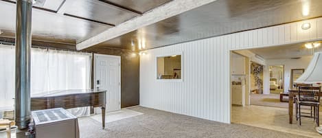 A spacious room with a large piano, a stone fireplace, and a view into another room with a dining area.