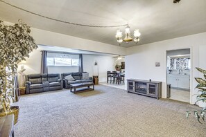 Una sala de estar con sofá, mesa de centro y chimenea. Se observa un comedor con sillas y una mesa, además de una cocina visible a través de una puerta abierta.