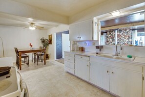 Una cocina con gabinetes blancos, una mesa de comedor con sillas, un ventilador de techo y un salpicadero de pared de piedra.