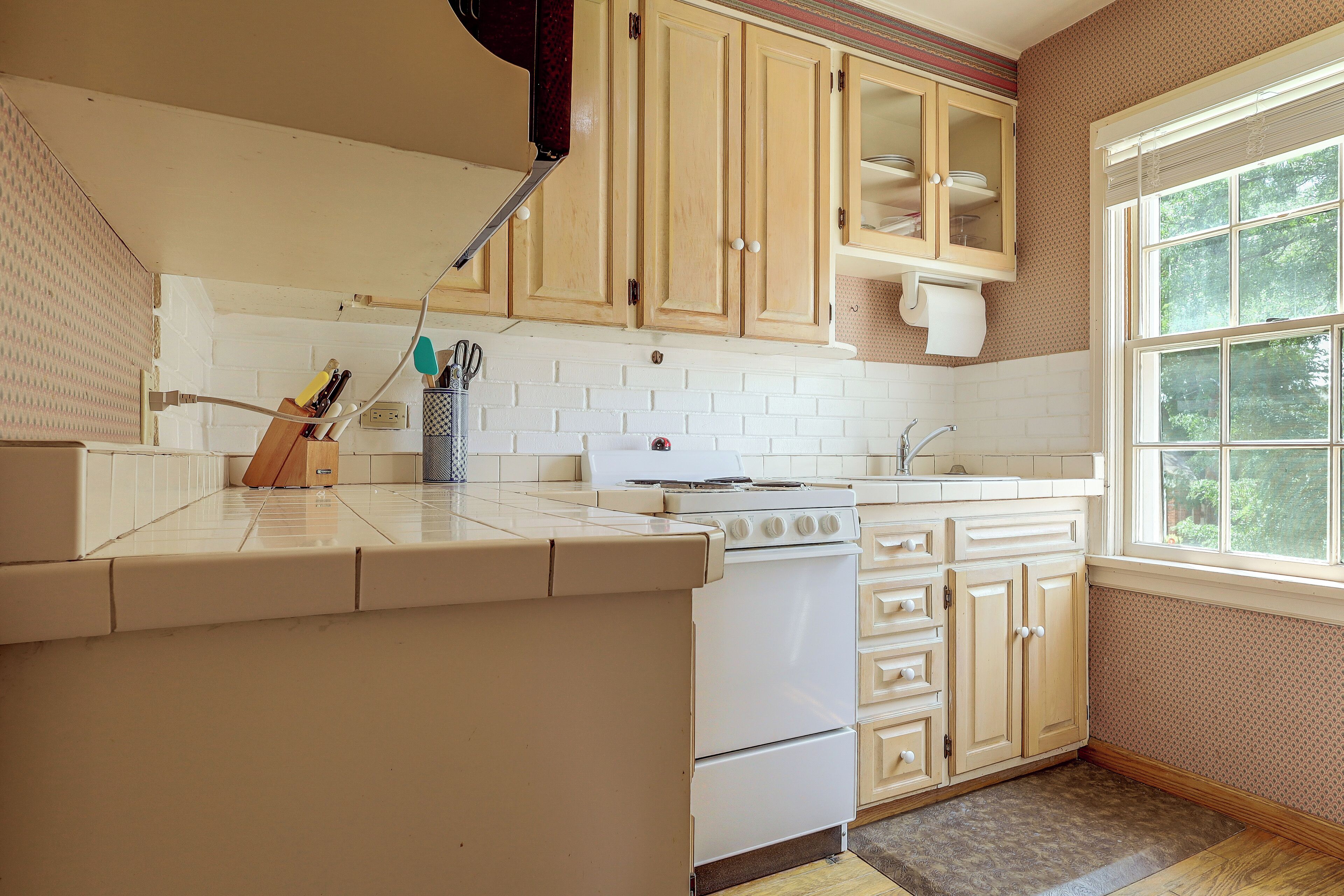 A kitchen with white cabinets, a stove, and a window.