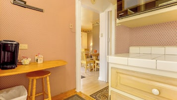 A small kitchenette with a coffee maker, a trash bin, and a wooden stool.