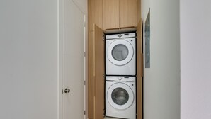 Ein kleiner Waschraum mit zwei übereinander gestapelten Waschmaschinen, einem Holzschrank und einer weißen Tür.