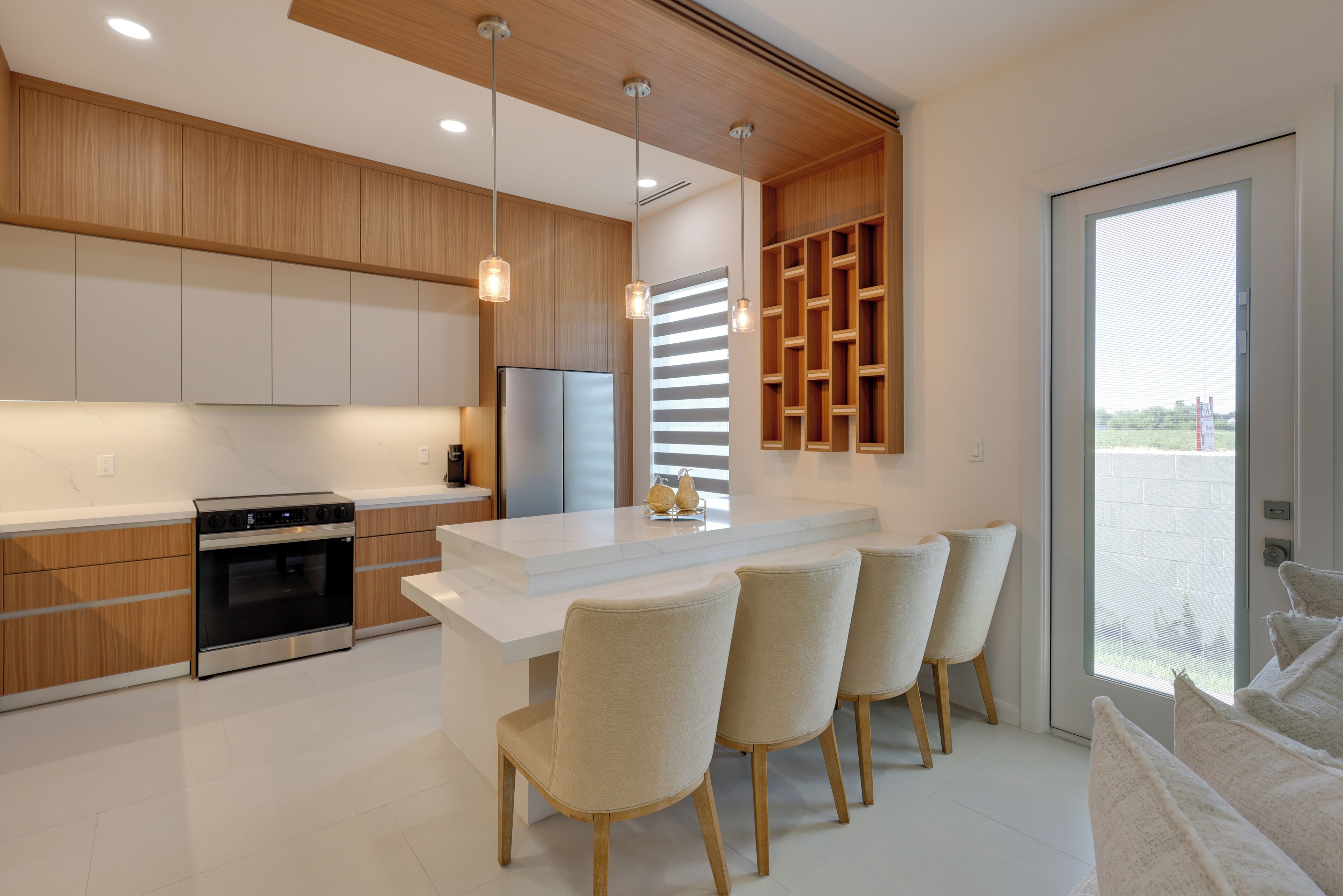 A modern kitchen with a central island, bar stools, built-in wooden cabinets, and a large window.