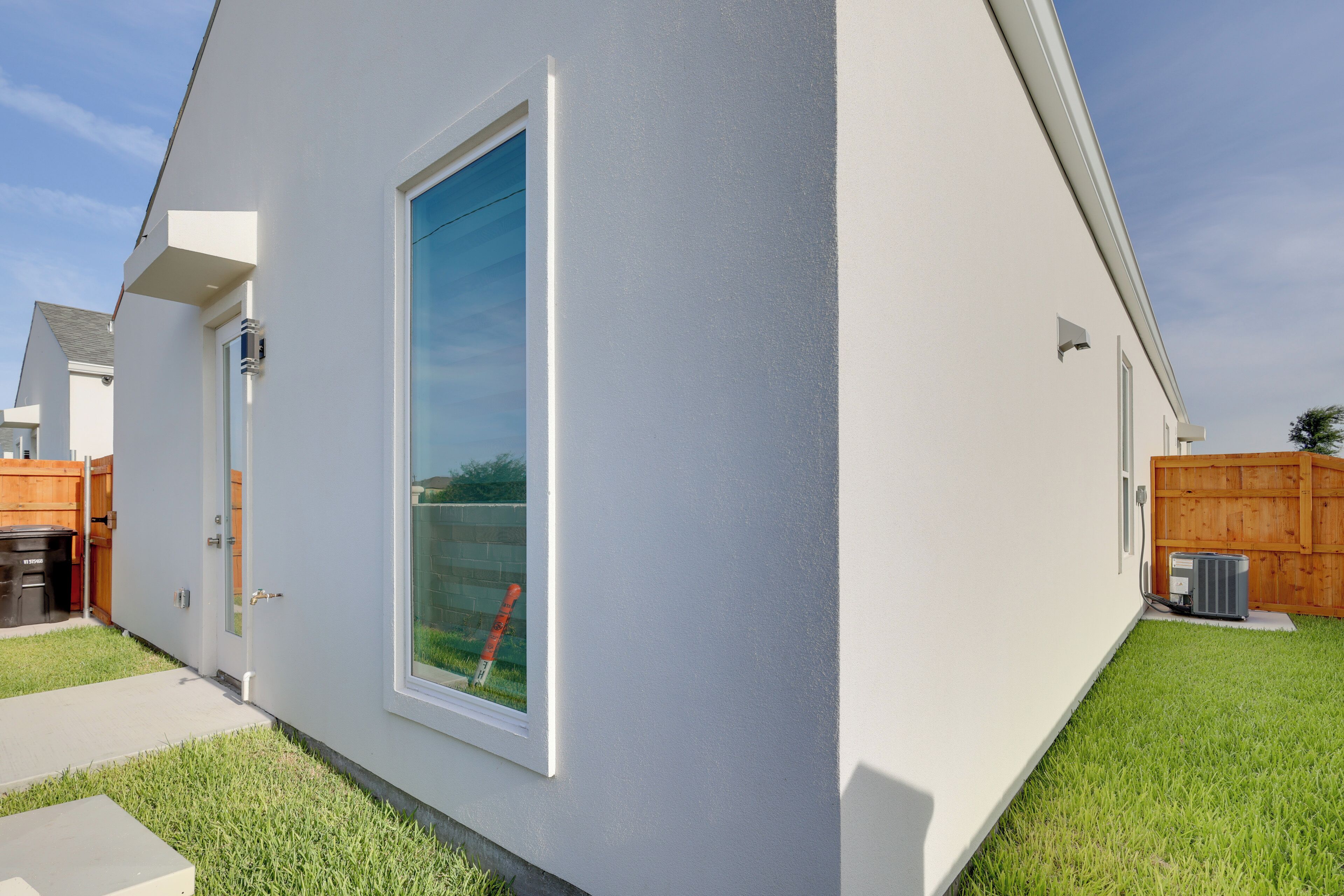 Una casa moderna con un ventanal grande, una puerta y un pequeño espacio exterior con cerca y un contenedor de basura.