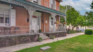 A two-story brick building with a white decorative fence, a front door, and a small porch area with steps leading up to it.