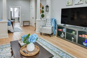 Un salón con televisor, una silla, una mesa de centro con un jarrón y flores, y una estantería.