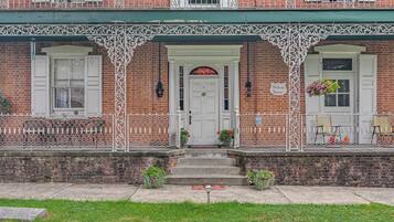 A brick building with a white door and windows, a green awning, and a sign that reads 'McCausland Mansion.'