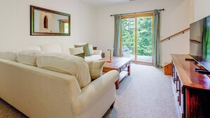 A living room with a sofa, a coffee table, and a television. There is a window with curtains and a view of trees outside. - Serene Wooded Cabin w/ Decks, 4 Mi to Dtwn Murphy (Murphy)