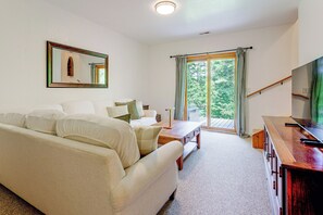 A living room with a sofa, a coffee table, and a television. There is a window with curtains and a view of trees outside. - Serene Wooded Cabin w/ Decks, 4 Mi to Dtwn Murphy (Murphy)