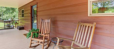 Un portico in legno con due sedie a dondolo, un tavolino e una pianta in vaso.
