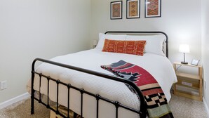 A neatly made bed with a metal frame, a bedside table with a lamp, and a wall with three framed pictures. - Serene Wooded Cabin w/ Decks, 4 Mi to Dtwn Murphy (Murphy)