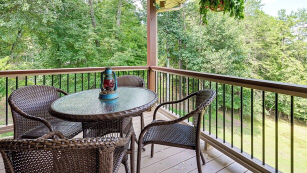 A covered outdoor area with a round table and wicker chairs, surrounded by a wooden railing. - Serene Wooded Cabin w/ Decks, 4 Mi to Dtwn Murphy (Murphy)