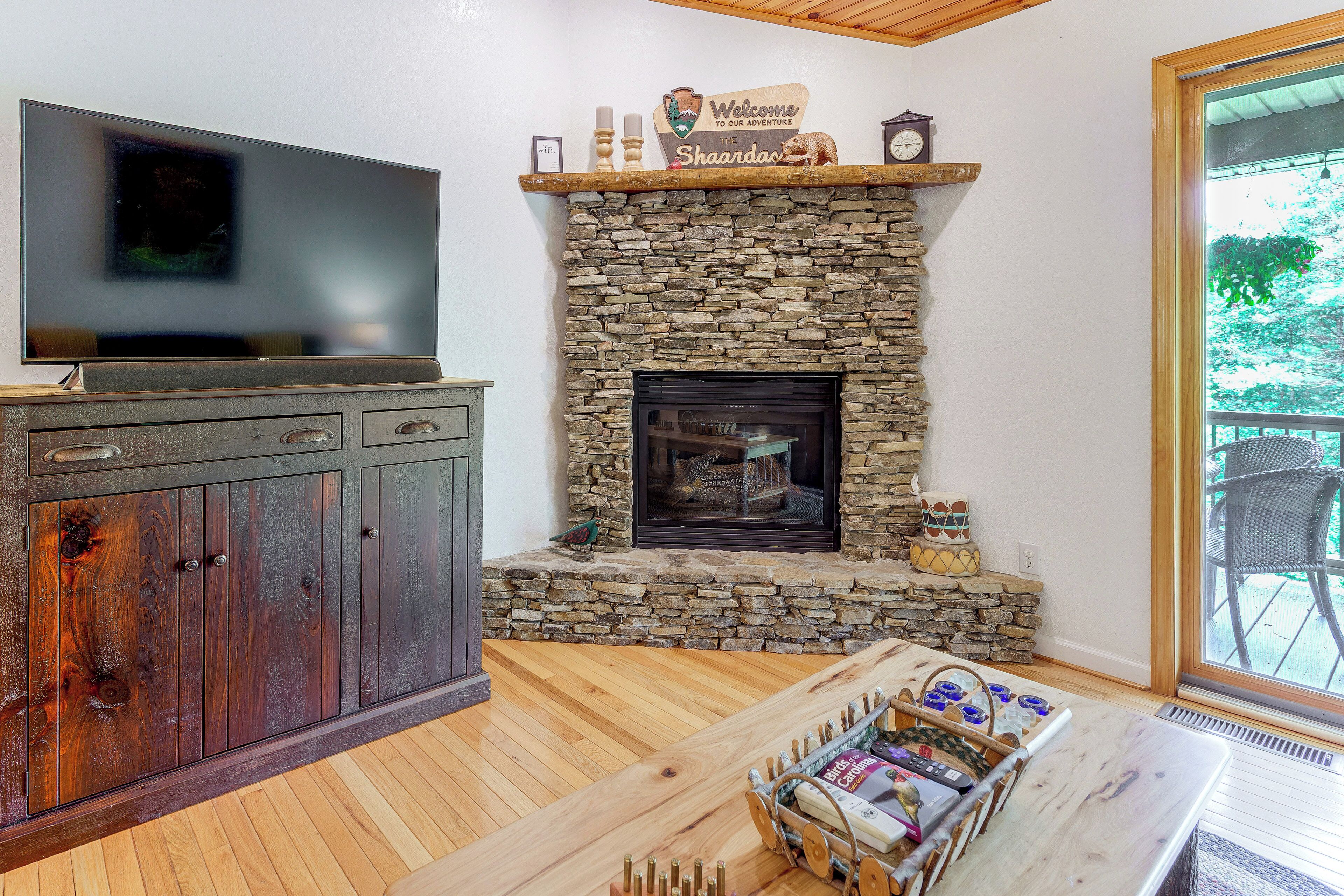 A stone fireplace with a sign above it, a television on a cabinet, and a wooden coffee table with items on it.