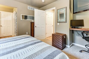 Ein Schlafzimmer mit einem Bett, einem Schreibtisch mit Computer, einem Spiegel und einem Kleiderschrank.