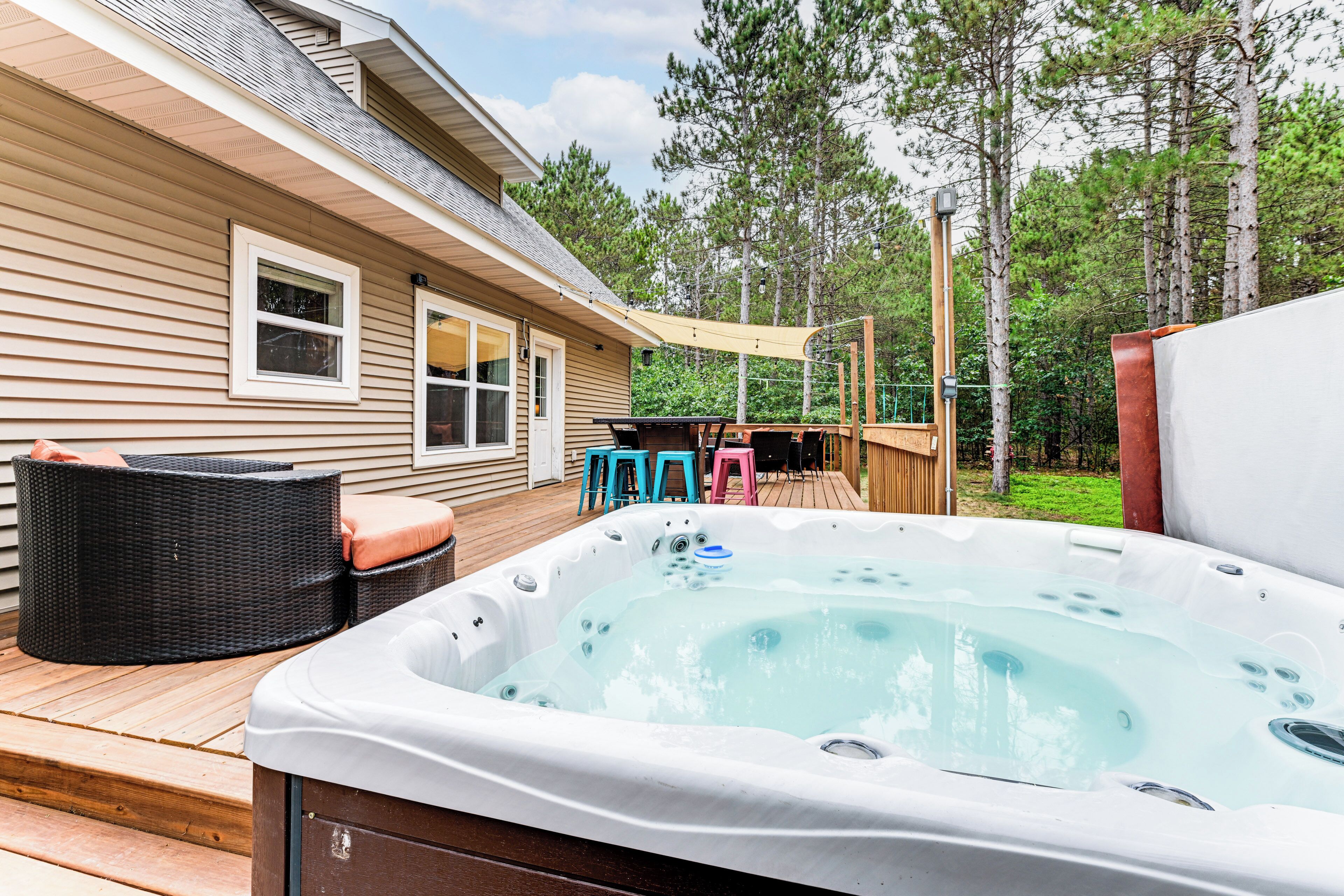 Un bain à remous sur une terrasse en bois, avec des meubles d’extérieur, et une maison en arrière-plan.
