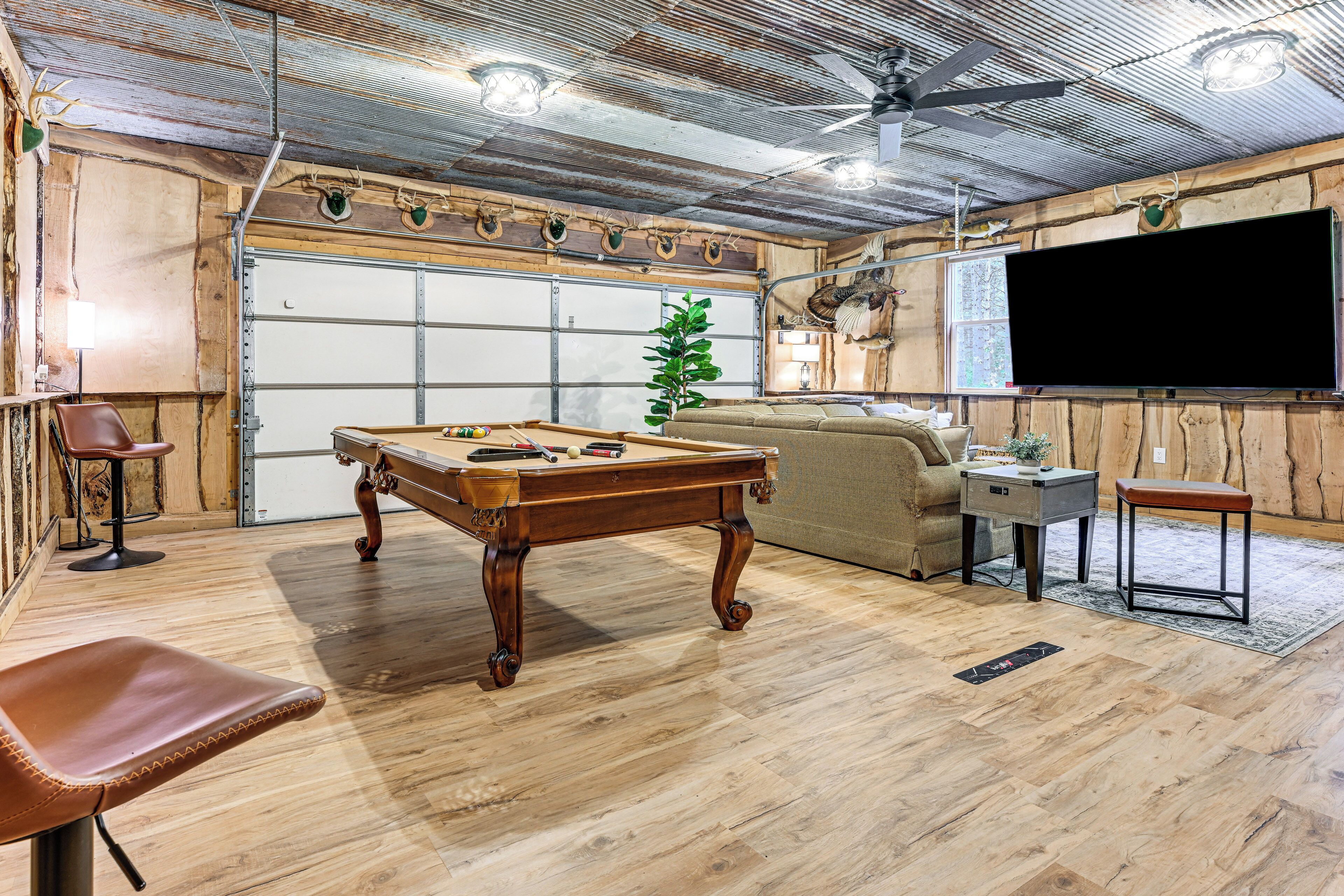 A room with a pool table, a sofa, a TV, and a ceiling fan.
