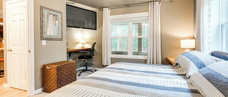 A bedroom with a bed, a desk, a chair, a television, and a window with curtains.