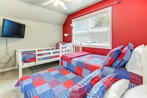 A bedroom with a red wall, a white bed, and a TV mounted on the wall.