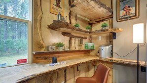 Interior de cabana com paredes de madeira rústica, área de bar com uma garrafa e dados, uma cadeira e uma placa que indica que a cabana é um lugar feliz.