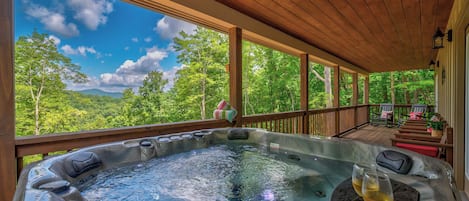Een hottub op een houten terras, met uitzicht op bos en bergen.