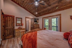 A bedroom with a wooden ceiling, a bed with a red blanket, a dresser, a mirror, and a television on a wooden cabinet. - Blue Ridge Views, Hot Tub! Murphy Mtn Cabin (Murphy)