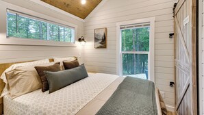 A bedroom with a bed, two windows, a painting, and a wooden ceiling. - Tiny Home - Fire Pit, Grill, Deck & View! (Otto)