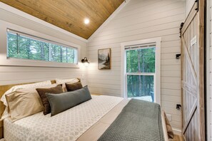 Ein Schlafzimmer mit einem Bett, zwei Fenstern, einem Gemälde und einer Holzbalkendecke.