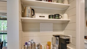 A kitchen with a coffee maker, tea kettle, and various kitchen utensils on shelves. - Tiny Home - Fire Pit, Grill, Deck & View! (Otto)