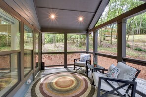 Eine überdachte Veranda mit Schaukelstuhl und Tisch, mit Blick auf ein bewaldetes Gebiet.