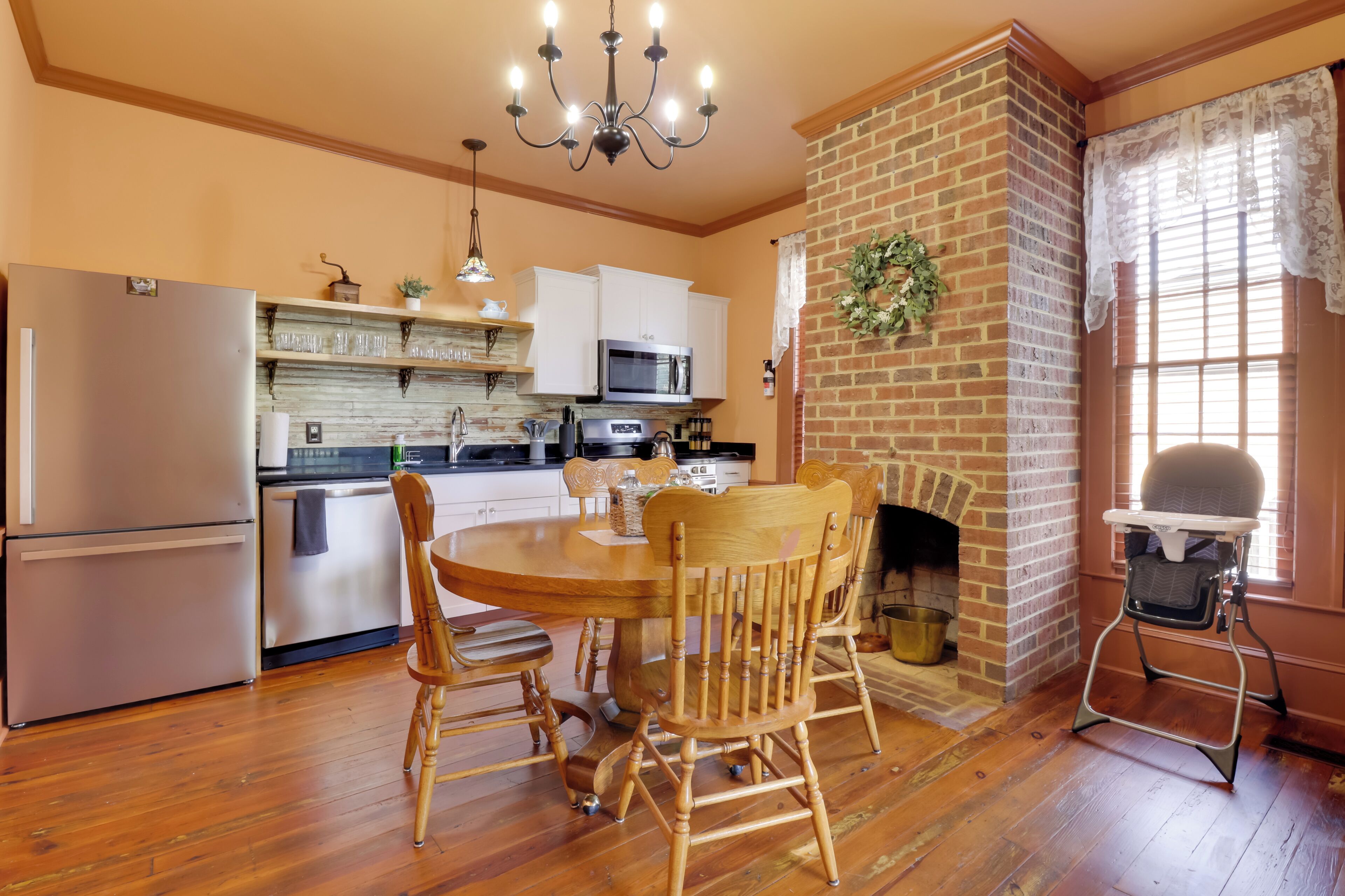 A kitchen with a brick fireplace, wooden dining table, and chairs, and a high chair.