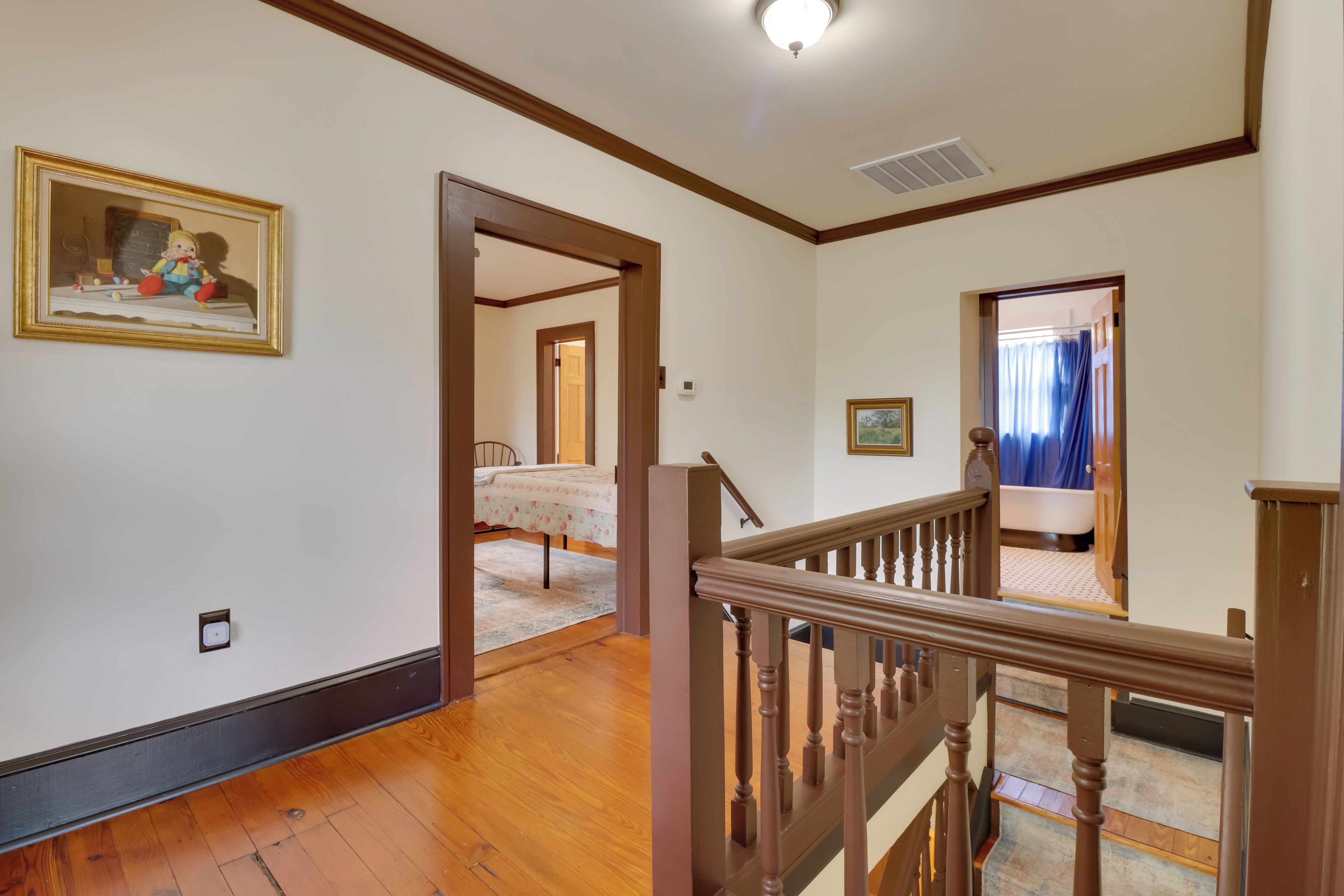 A spacious room with hardwood floors, a wooden staircase, and a bed with a floral bedspread.